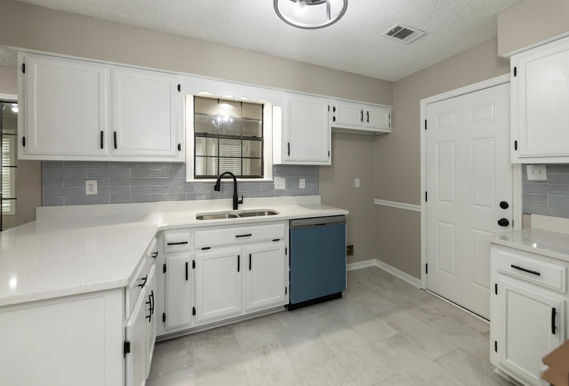 Kitchen featuring dishwashing machine, light stone counters, white cabinetry, a textured ceiling, and backsplash