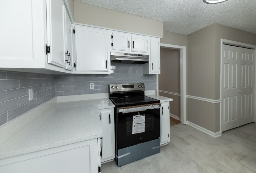 Kitchen featuring stainless steel electric range oven, white cabinetry, decorative backsplash, and a textured ceiling