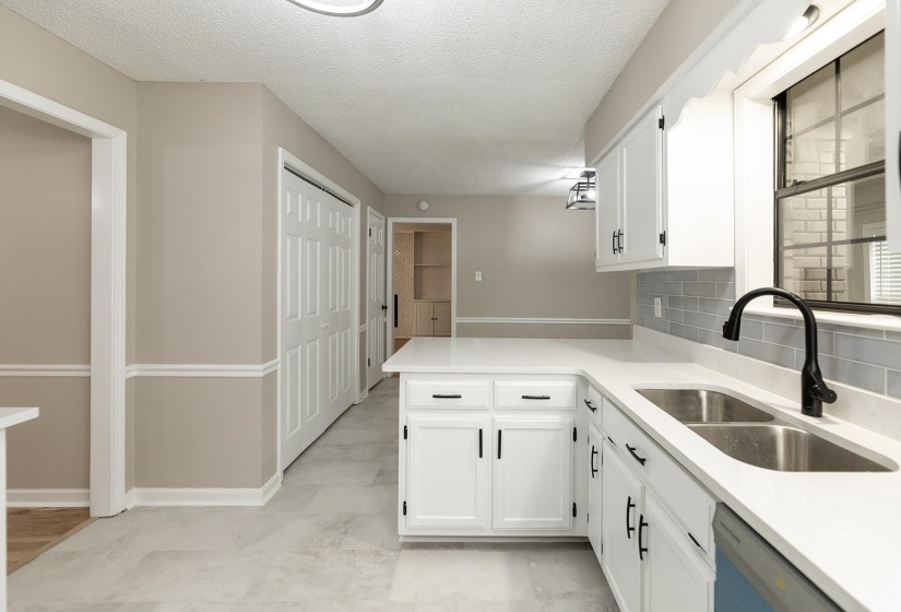 Kitchen with a textured ceiling, white cabinets, dishwashing machine, a peninsula, and light stone countertops