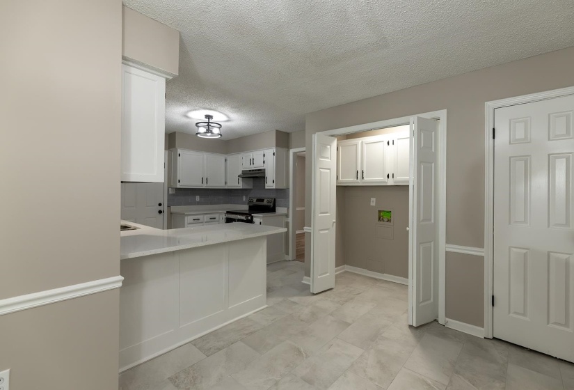 Kitchen with white cabinets, a textured ceiling, stainless steel range with electric cooktop, and a peninsula