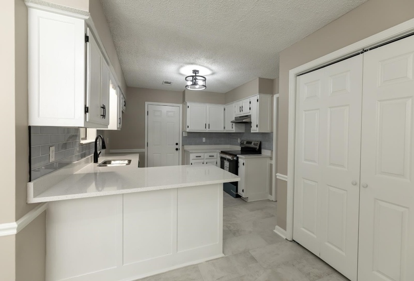 Kitchen with white cabinetry, stainless steel electric range oven, a peninsula, a textured ceiling, and light stone countertops