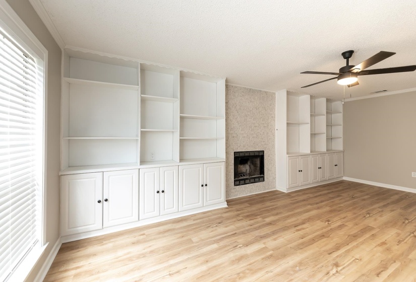 Unfurnished living room featuring crown molding, ceiling fan, light wood finished floors, a large fireplace, and a textured ceiling