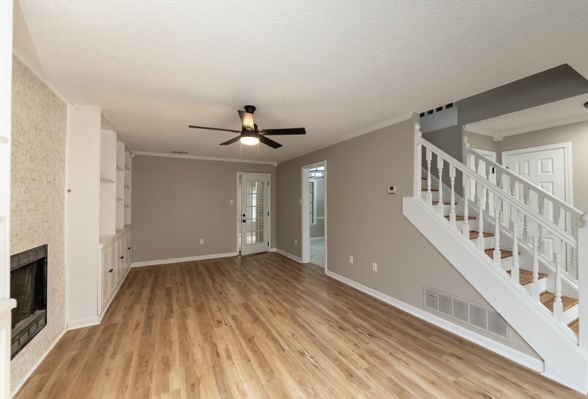 Unfurnished living room featuring a ceiling fan, light wood-style floors, a fireplace, a textured ceiling, and ornamental molding