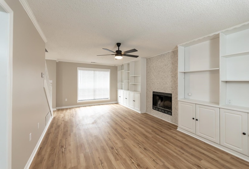 Unfurnished living room featuring ceiling fan, built in features, light wood finished floors, a textured ceiling, and a tile fireplace