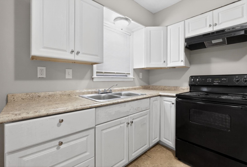 Kitchen with black range with electric stovetop, white cabinets, exhaust hood, and light countertops