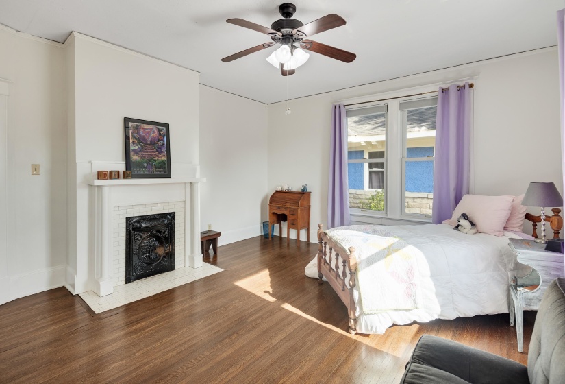 Bedroom featuring wood finished floors, a fireplace, and a ceiling fan