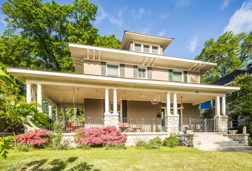 Rear view of property featuring a lawn, a large porch, stone siding, and stucco siding