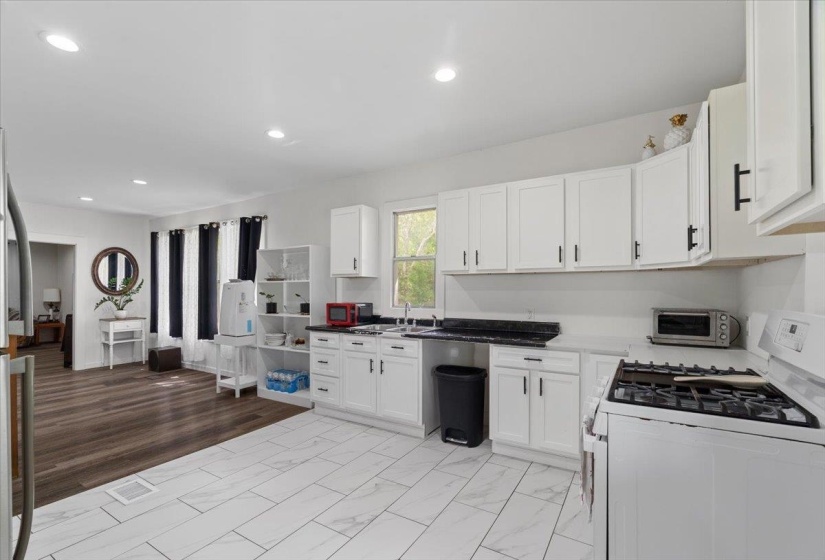 Kitchen featuring white gas stove, white cabinets, recessed lighting, light marble finish flooring, and freestanding refrigerator