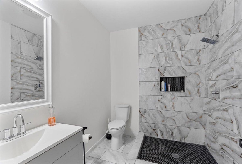 Bathroom featuring vanity, light marble finish floors, and a tile shower