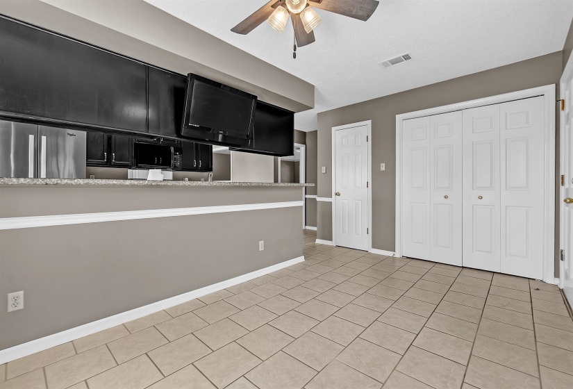 Kitchen with dark cabinets, ceiling fan, light countertops, stainless steel fridge, and light tile patterned flooring