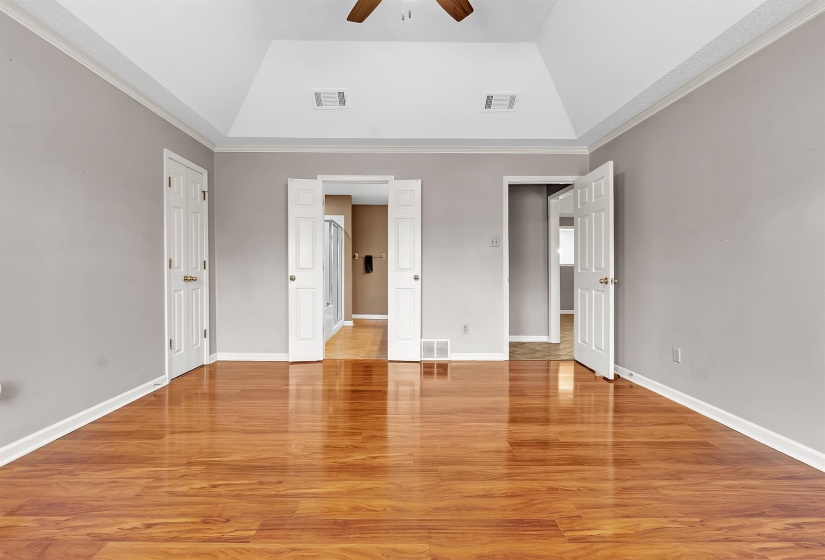 Unfurnished bedroom featuring light wood-type flooring, ornamental molding, a ceiling fan, and vaulted ceiling