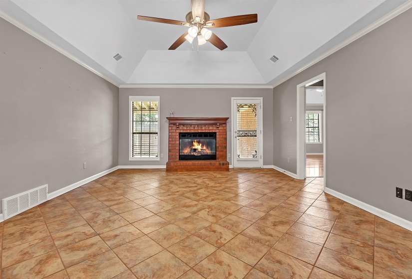 Unfurnished living room featuring a ceiling fan, ornamental molding, a brick fireplace, lofted ceiling, and light tile patterned flooring
