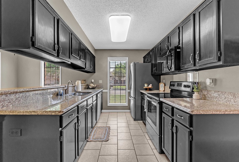 Kitchen featuring dark cabinetry, stainless steel appliances, light stone countertops, a textured ceiling, and light tile patterned floors
