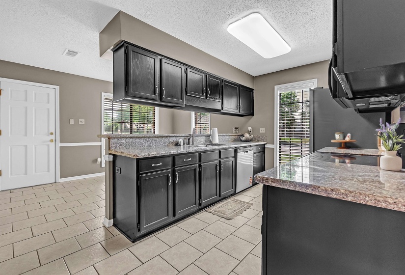 Kitchen with dark cabinets, a textured ceiling, light stone countertops, stainless steel appliances, and light tile patterned flooring