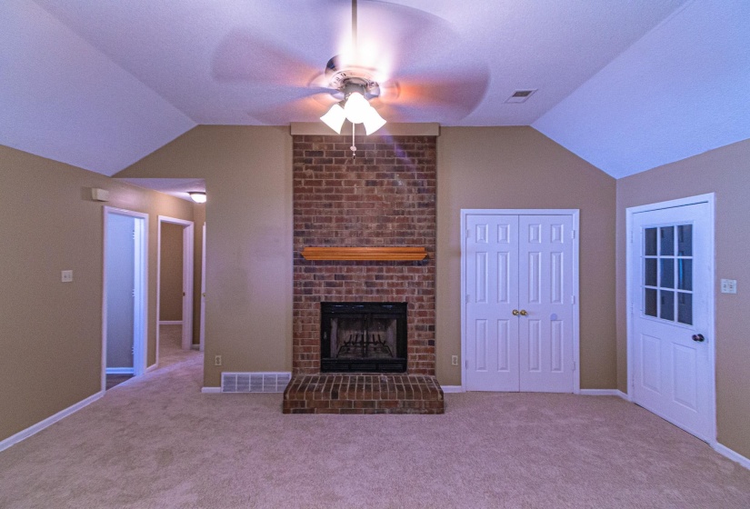 Unfurnished living room featuring vaulted ceiling, ceiling fan, a brick fireplace, and light carpet