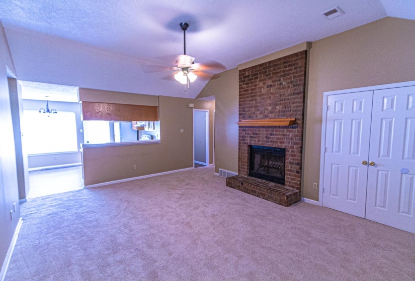 Unfurnished living room with vaulted ceiling, a ceiling fan, a fireplace, and carpet floors