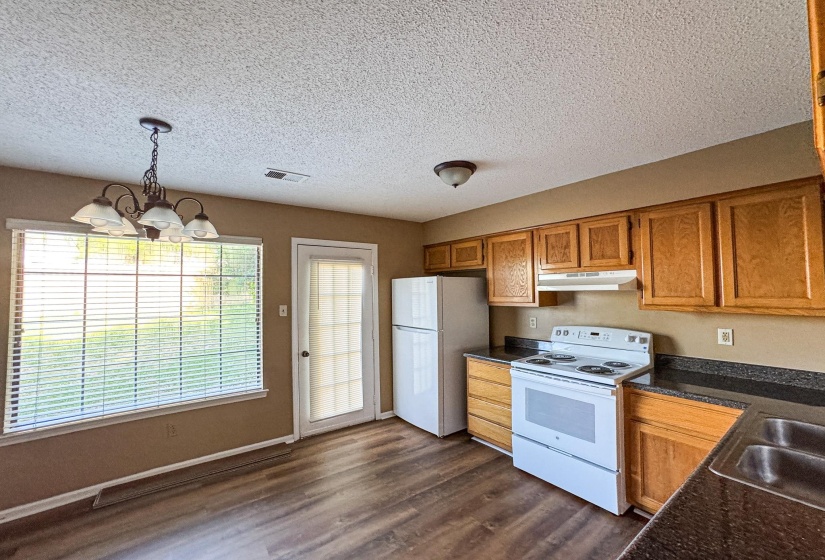 Kitchen featuring white appliances, a chandelier, wood finish cabinets, dark countertops, and dark wood-style floors