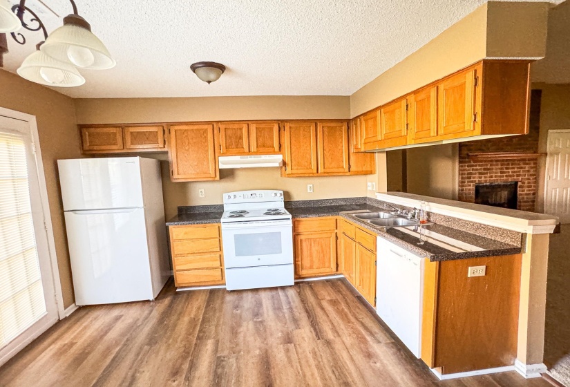 Kitchen with white appliances, dark countertops, hanging light fixtures, dark wood finished floors, and a textured ceiling