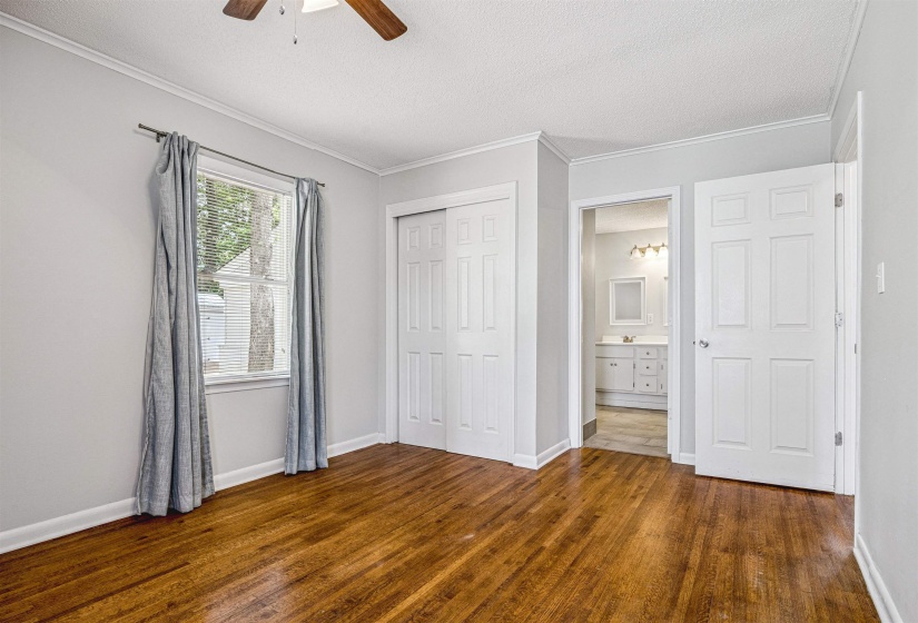 Unfurnished bedroom featuring a textured ceiling, crown molding, a closet, dark wood-style flooring, and a ceiling fan