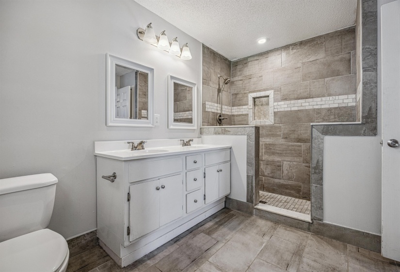 Full bath featuring double vanity, walk in shower, and a textured ceiling
