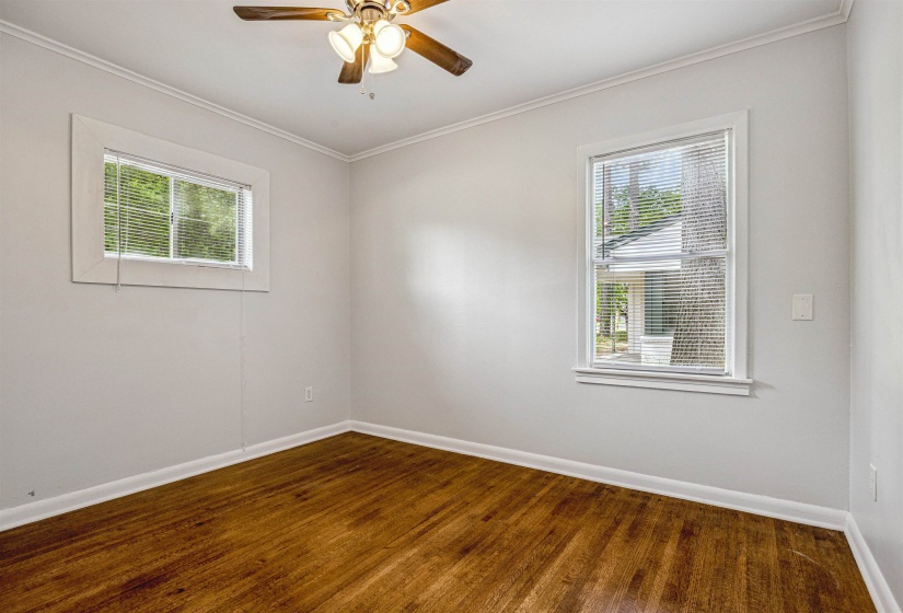 Empty room featuring dark wood-type flooring, ceiling fan, and ornamental molding