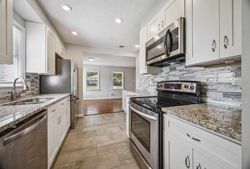 Kitchen with stainless steel appliances, light stone countertops, white cabinetry, a textured ceiling, and recessed lighting