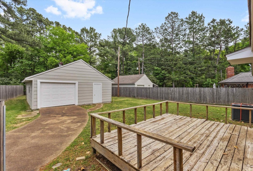 Wooden deck with a fenced backyard, an outdoor structure, a detached garage, and concrete driveway