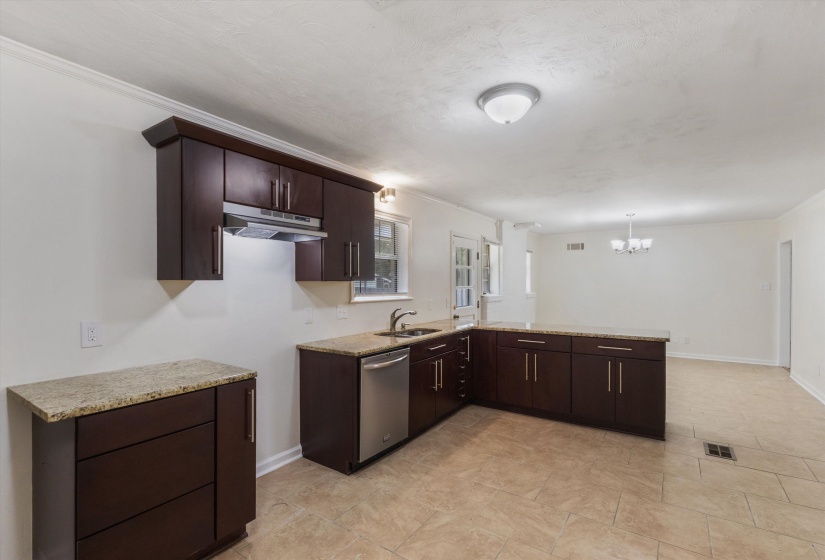 Kitchen with dark wood finish cabinets, a peninsula, ornamental molding, dishwasher, and light stone counters