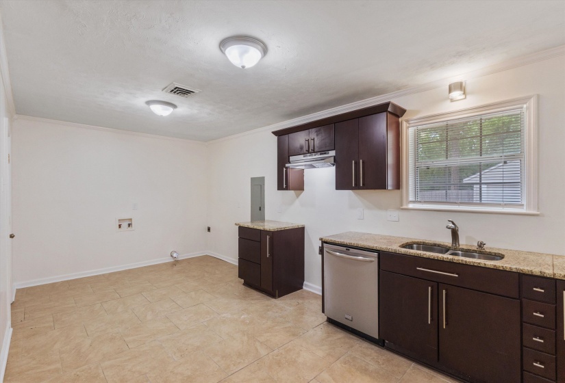 Kitchen featuring dark wood finish cabinetry, stainless steel dishwasher, light stone counters, and ornamental molding