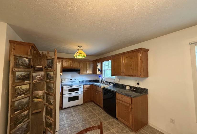 Kitchen with double oven range, wood finish cabinetry, dark countertops, black dishwasher, and a textured ceiling