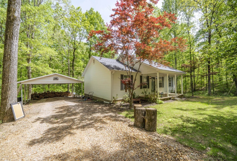 View of front facade featuring covered porch, a carport, driveway, roof with shingles, and view of scattered trees