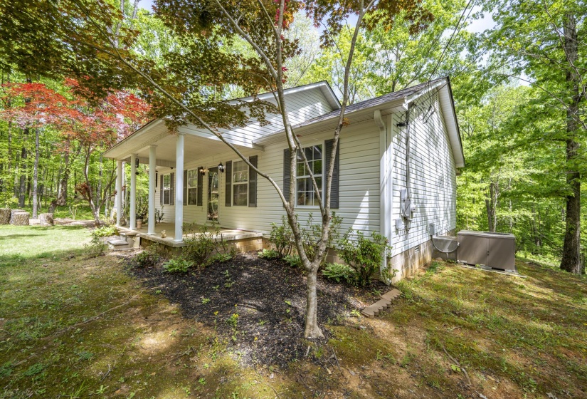 View of home's exterior with a porch, a lawn, and view of wooded area
