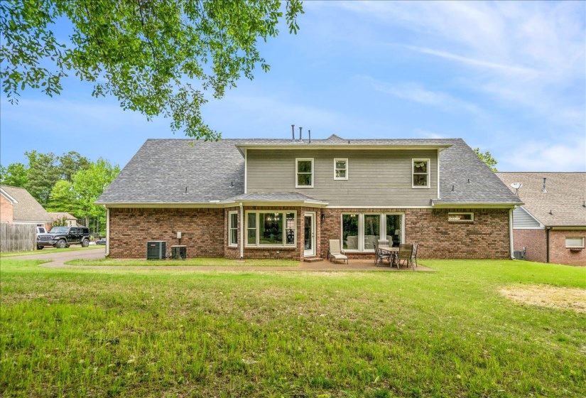 Back of property featuring a yard, brick siding, a patio area, and a shingled roof