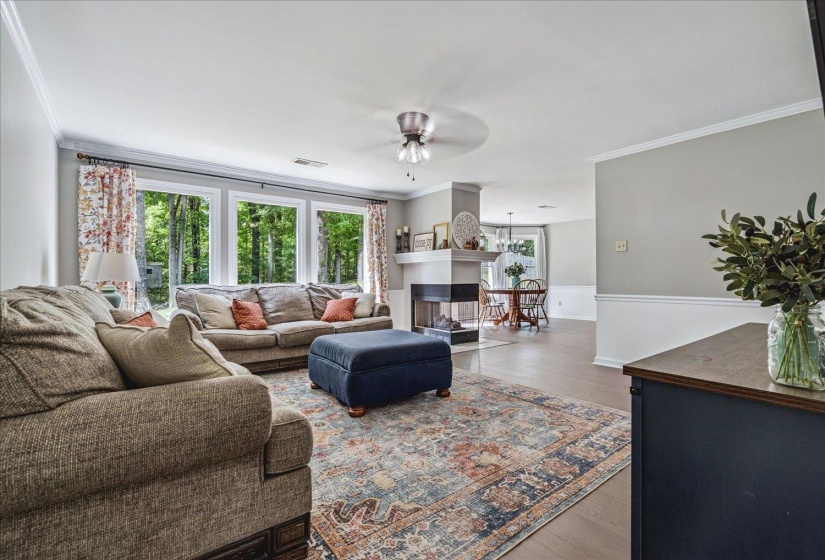 Living room with wood finished floors, ceiling fan, ornamental molding, and a multi sided fireplace