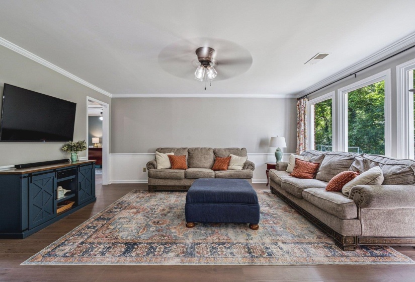 Living room featuring dark wood-type flooring, crown molding, and ceiling fan