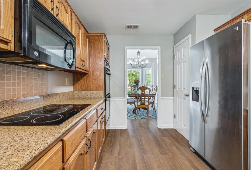 Kitchen with black appliances, a wainscoted wall, dark wood-type flooring, light stone countertops, and hanging lights