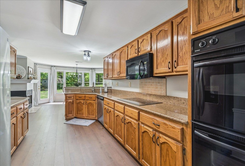 Kitchen with black appliances, wood finish cabinetry, a peninsula, and light wood-style flooring