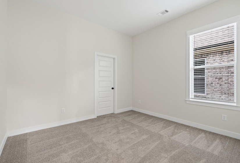 Neutral wall paint with textured carpeting, a single window featuring blinds, a multi-panel door, and white baseboards