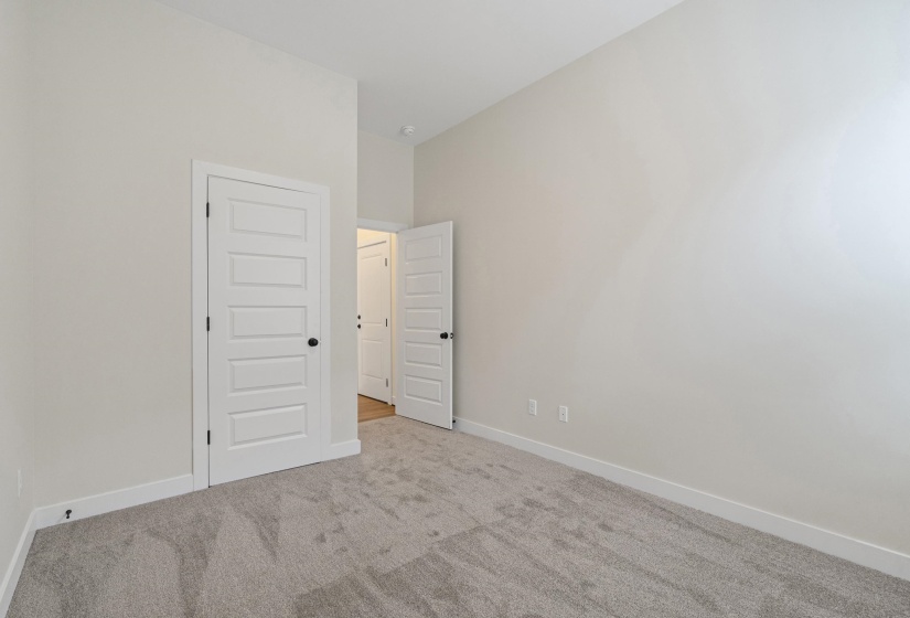 Neutral tone walls, grey textured carpeting, white baseboards, and white paneled doors with black hardware