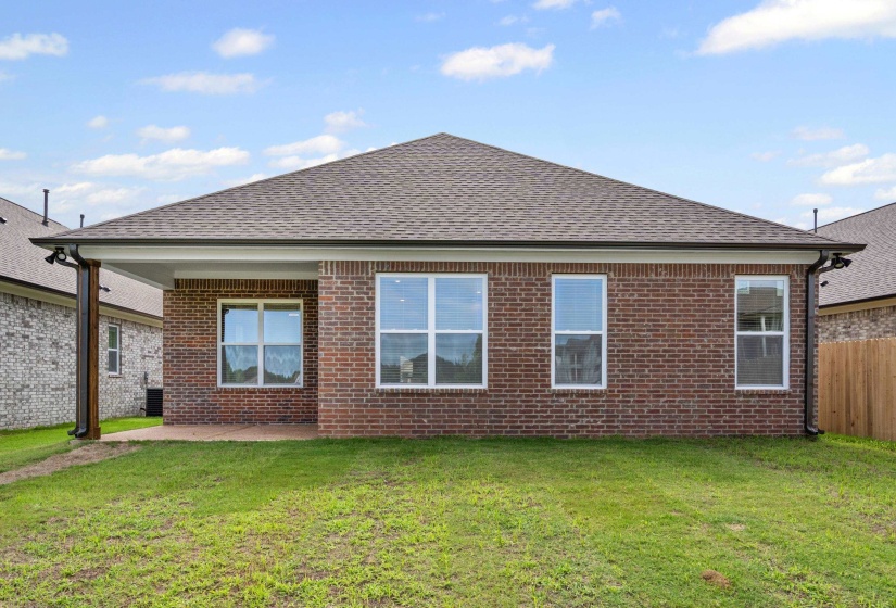 Red brick exterior with multiple windows, a covered patio area with a wood-wrapped column, and a spacious green lawn