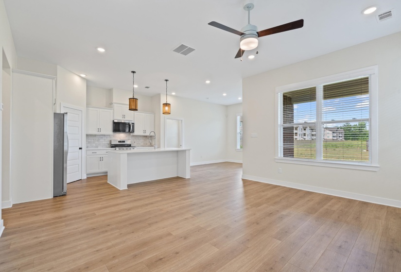 Open-concept interior featuring wood-finish flooring, a white kitchen island, and stainless steel appliances