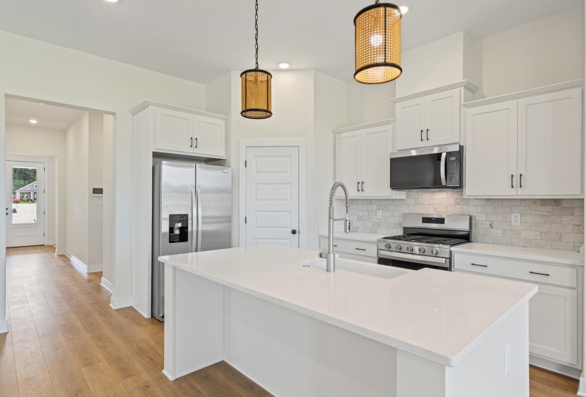Kitchen featuring a central island with an undermount sink, stainless steel appliances, white cabinetry, wood-finish flooring, and pendant lighting fixtures