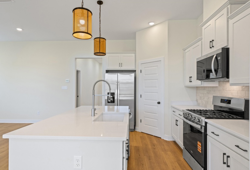 Modern kitchen featuring an expansive island with an integrated sink, white cabinetry, stainless steel appliances, and wood-finish flooring