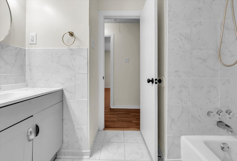 Bathroom featuring light marble finish flooring, vanity, shower / bathtub combination, and tile walls