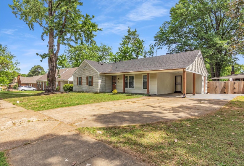 Ranch-style house with concrete driveway, a carport, roof with shingles, a front yard, and brick siding