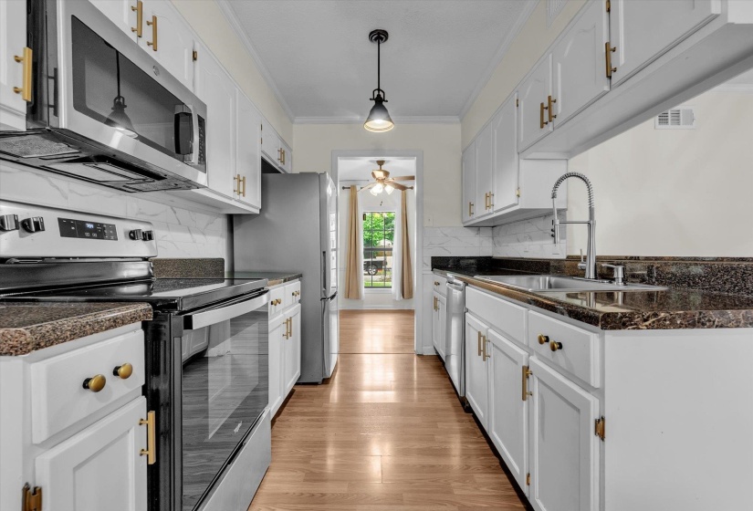 Kitchen featuring stainless steel appliances, crown molding, white cabinetry, decorative backsplash, and light wood-type flooring