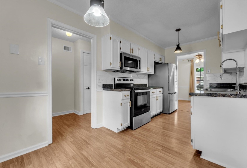 Kitchen with pendant lighting, stainless steel appliances, white cabinetry, tasteful backsplash, and ornamental molding