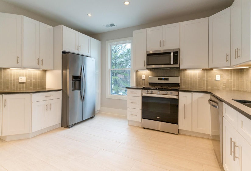 Kitchen featuring backsplash, appliances with stainless steel finishes, white cabinetry, recessed lighting, and dark stone counters