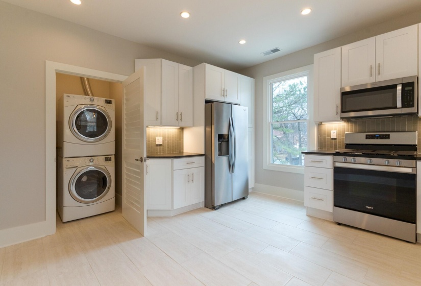 Kitchen with appliances with stainless steel finishes, white cabinets, stacked washer / drying machine, recessed lighting, and tasteful backsplash