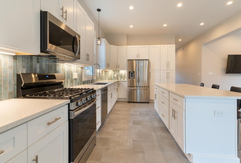 Kitchen featuring appliances with stainless steel finishes, a kitchen breakfast bar, white cabinets, backsplash, and light stone counters